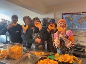 Group picture of volunteer kitchen team prepping butternut squash featuring artist and performer Victoria Melody and Community Champion, Sue Mechen,